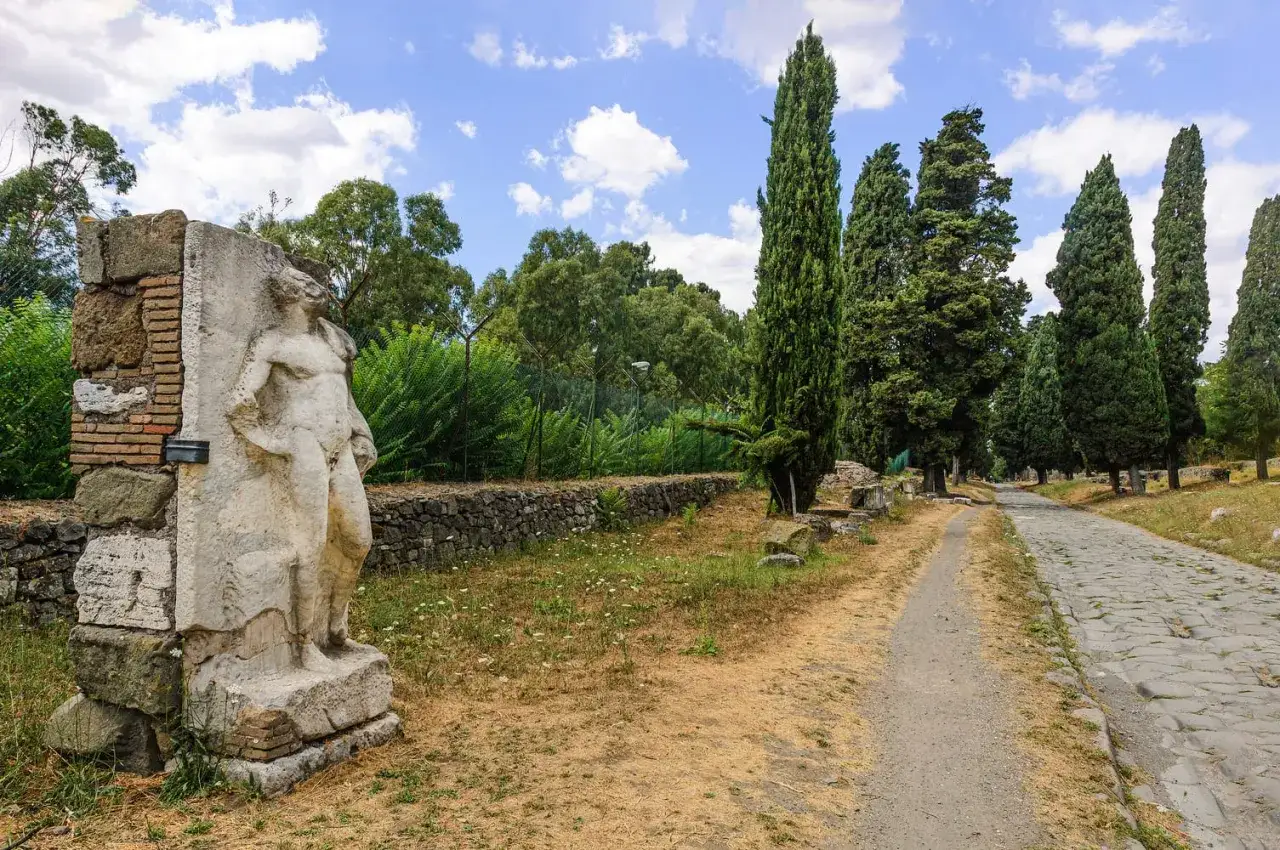 Vestige de la via antica Roma, une statue antique se dresse près d'une route pavée bordée de cyprès.