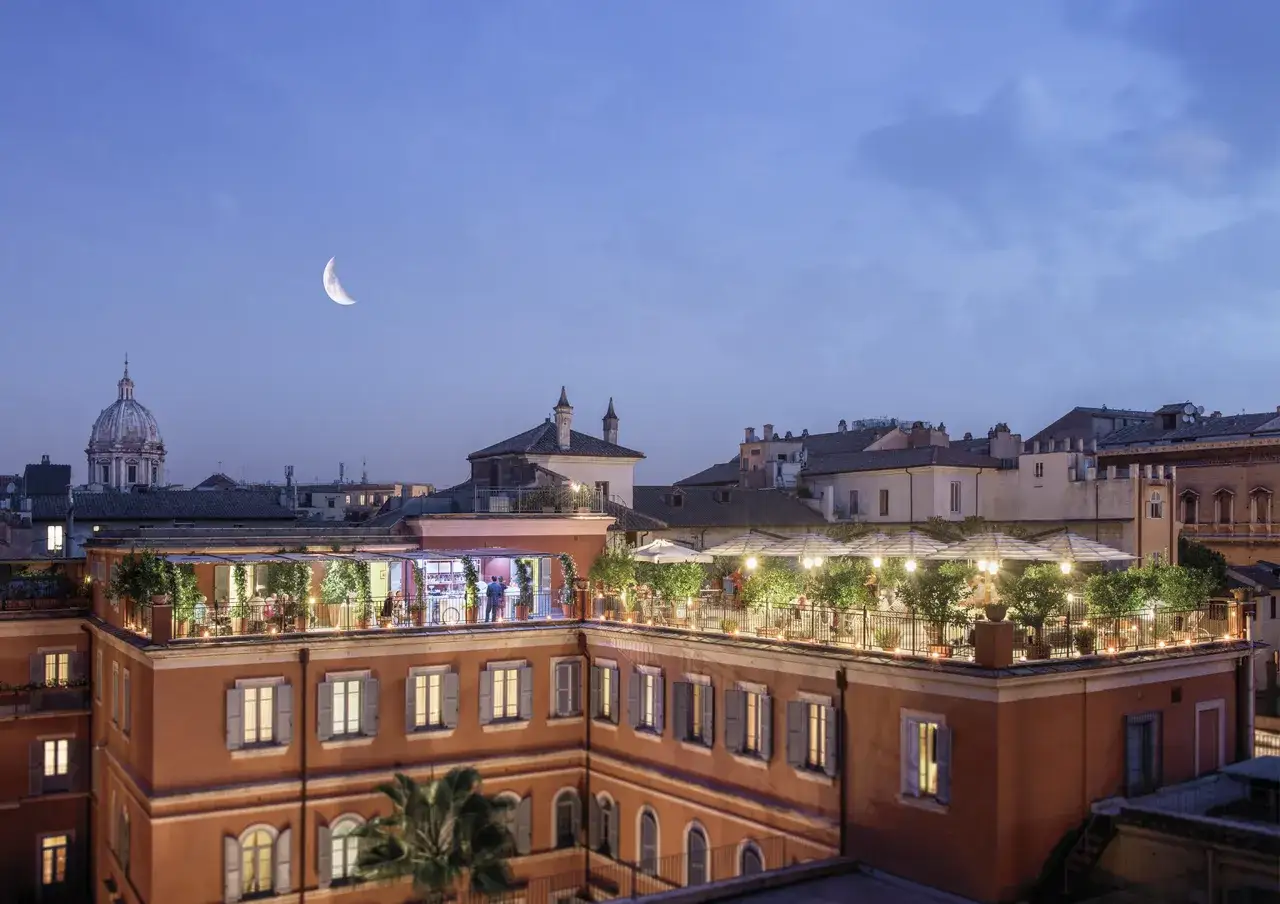 Vue du toit-terrasse animé du hotel Ponte Sisto Rome sous un ciel crépusculaire avec une lune en croissant.