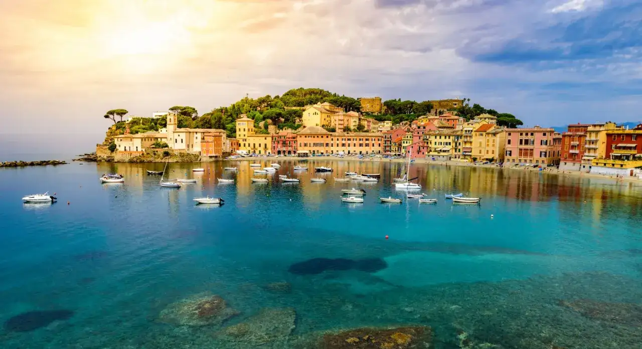 Vue pittoresque de la baie de Sestri Levante en Italie, avec des maisons colorées, des bateaux dans l'eau turquoise et un ciel ensoleillé.