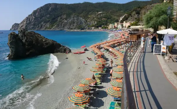 Plage animée à Moneglia, Italie, avec des parasols rayés, des baigneurs dans la mer turquoise et des collines verdoyantes en arrière-plan.